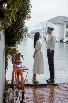 a man and woman standing under an umbrella in the rain next to a orange bike