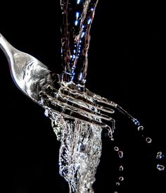 water pouring out of a silver fork into the air with bubbles coming from it on a black background