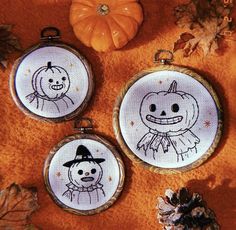 three cross stitch halloween ornaments with pumpkins in the background