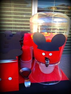 a red mickey mouse coffee maker sitting on top of a table next to some cups