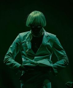 a woman with green hair and glasses standing in the dark