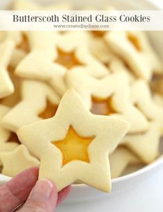 a hand holding a star shaped cookie in front of a white bowl filled with cookies