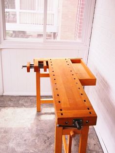 a wooden bench sitting in front of a window next to a white brick wall and floor