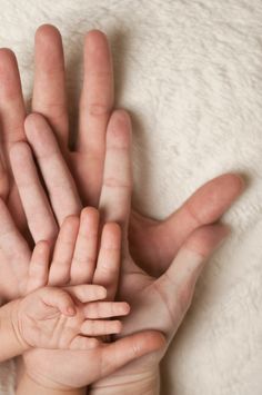 several hands are stacked together on a white blanket, with one hand extended up to the camera