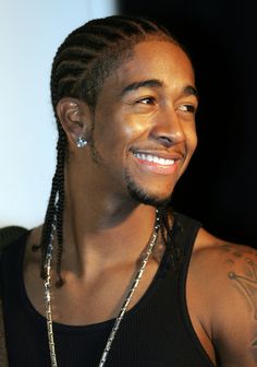 a man with dreadlocks smiles at the camera while wearing a black tank top