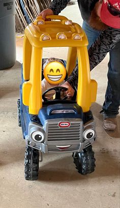 a little boy riding on top of a toy truck with a face painted on it