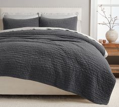 a bed with a gray quilt on top of it next to a table and window