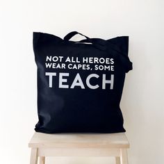 a black tote bag sitting on top of a wooden chair next to a white wall