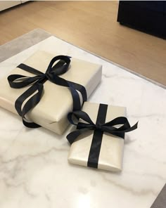 two wrapped presents sitting on top of a marble table with black ribbon tied around them