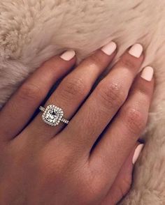 a woman's hand with a diamond ring on her finger and a fur rug in the background