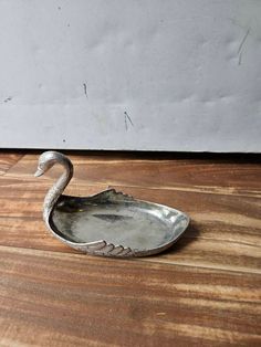 a metal swan shaped dish sitting on top of a wooden table