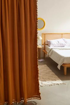 a bed sitting next to a window covered in orange drapes on top of a wooden frame