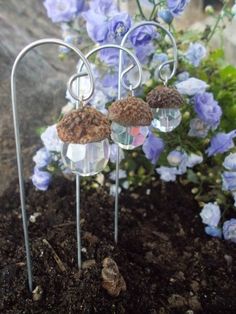 three glass vases are sitting on top of some dirt and blue flowers in the background