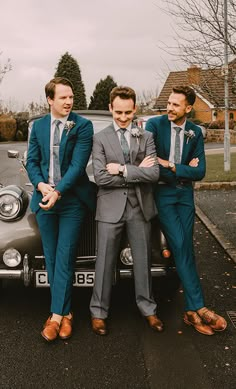 three men in suits standing next to an old car with their arms around each other