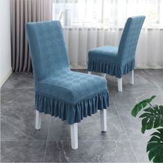 two blue chairs with ruffled covers on them in front of a window and potted plant