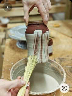 a person is painting a vase with white and brown stripes on the outside of it