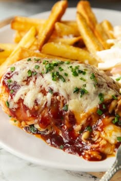 a white plate topped with chicken parmesan covered in sauce next to french fries