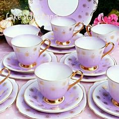 purple and gold tea set with matching saucers, cups and saucers on a pink tablecloth