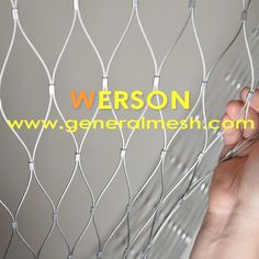 a hand holding a piece of wire next to a white fence with the word, person on it