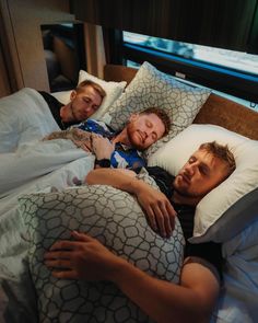 two men laying in bed with pillows on them