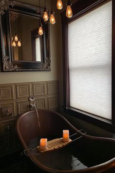 a bath tub sitting under a bathroom mirror next to a window with light bulbs hanging from it