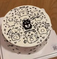 a white cake decorated with black cats and bears on it's side, sitting on top of a wooden table