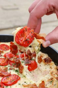 a person is taking a slice of pizza with tomatoes and bacon on it from a skillet