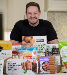 a man sitting at a kitchen counter surrounded by packaged food and smiling for the camera