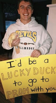 a young man holding a sign that says i'd be lucky duck to go to prom with you