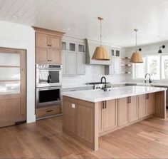 a large kitchen with wooden floors and white walls, two ovens, an island in the middle