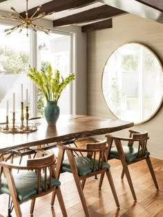 a dining room table with green chairs and a large round window in the back ground