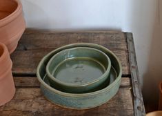 three green bowls sitting on top of a wooden table next to potted planters