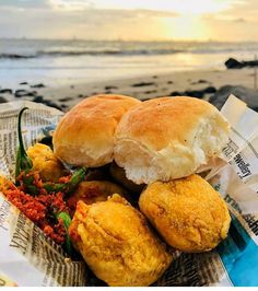 two rolls and some food on a newspaper near the ocean