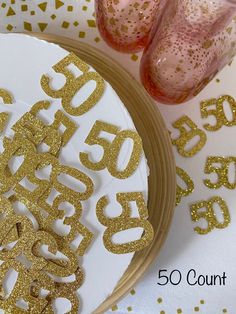 a white plate topped with gold glitter numbers next to pink glasses and confetti