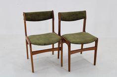 two wooden chairs with green upholstered seats on each side, one is facing the other