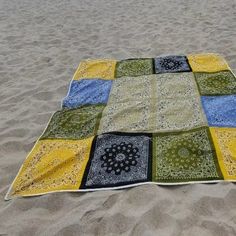 a patchwork blanket is laying on the sand at the beach in front of the ocean