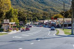 cars are driving down the street in front of shops and mountains with power lines above them