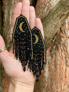 a pair of black and gold beaded earrings in front of a tree with the word love written on it