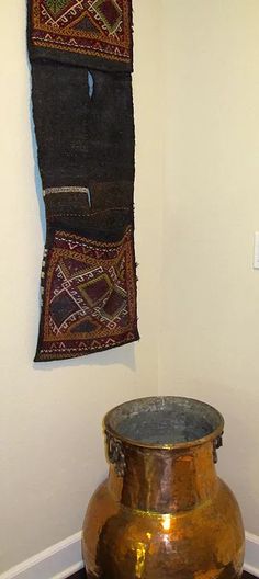 a large metal vase sitting on top of a wooden table next to a wall hanging