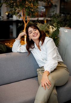 a woman sitting on top of a gray couch next to a potted green tree