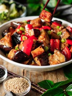 a bowl filled with tofu and vegetables on top of a wooden table next to some chopsticks