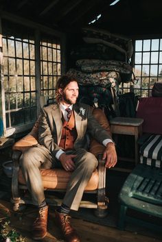 a man in a suit and tie sitting on a chair with his legs crossed, wearing brown boots