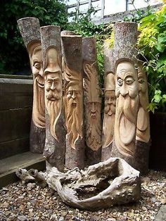 four carved wooden faces are sitting on the rocks in front of some plants and trees