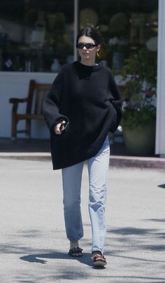 a woman in black sweater and jeans walking down the street