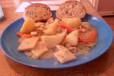 a blue plate topped with meat and veggies covered in gravy next to bread