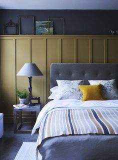 a bedroom with yellow and blue walls, striped bedspread, gray headboard