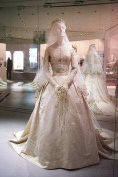 a white wedding dress on display in a glass case with mannequins behind it