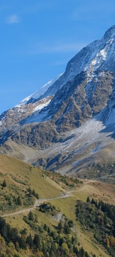 a mountain covered in snow and trees with a road going through the valley next to it