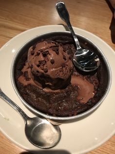 an ice cream sundae on a white plate with spoons next to the bowl