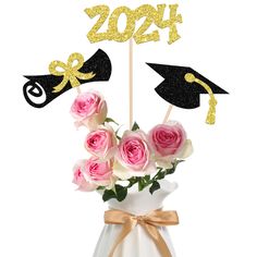 a vase filled with pink roses and two graduation hats